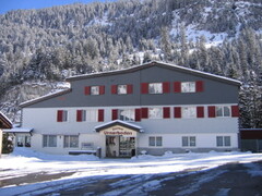 Das Gasthaus Urnerboden mit roten Fensterlaeden, dahinter verschneiter Wald.