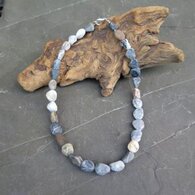 Eine Steinkette liegt auf einem knorrigen Holzstück.